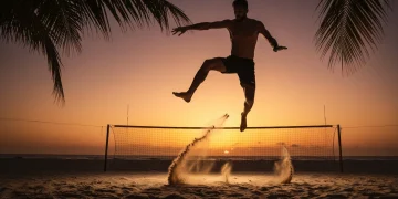 Jogador de futevôlei executa um 'shark attack' em quadra de areia ao pôr do sol, mostrando a habilidade técnica e a atmosfera vibrante do esporte.