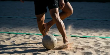Fotografia profissional de um jogador de futevôlei controlando a bola com precisão na areia, com iluminação dramática destacando a ação e detalhes da quadra.