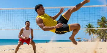 Dynamic footvolley action on a sunny beach court with two male athletes in mid-game.